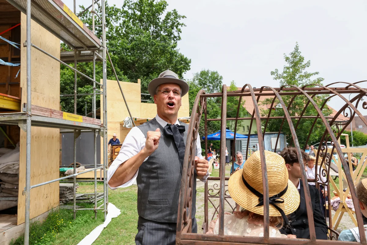 Andres Ulmann als Julius Maggi, der Werbung für seine soeben erfundene Suppe macht. Als erfolgreicher Fabrikherr wird er mit Zylinder und Wohlstandsbauch auftreten. Ein Mann mit Hut steht und gestikuliert.